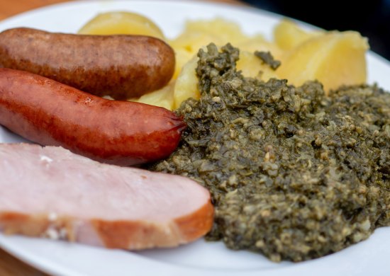 Grünkohl mit Salzkartoffeln, Pinkelwurst und Kassler auf einem Teller. 