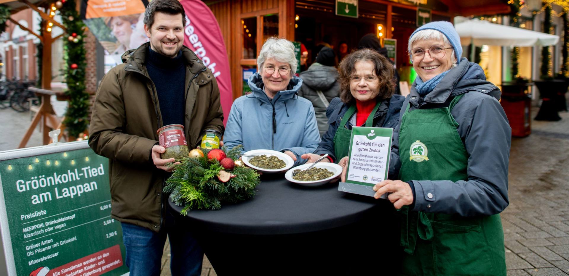 BU: Gesch&auml;ftsf&uuml;hrer Philipp Meerpohl, dessen Fleischerei den Gr&uuml;nkohleintopf f&uuml;r die &bdquo;Gr&ouml;&ouml;nkohl-Tied&ldquo; vollst&auml;ndig spendete, gemeinsam mit Dr. Beate Jonas, Vorstandsvorsitzende des Hospizdienstes, und Beate Weidewitsch, Koordinatorin und Beraterin vor Ort. Am Stehtisch mit dem servierten Gr&uuml;nkohleintopf sind sie mit Silke Fennemann, Gesch&auml;ftsf&uuml;hrerin der OTM und Veranstalterin der Gr&ouml;&ouml;nkohl-Tied am Lappan, zu sehen. Die gesamten Erl&ouml;se gehen als Spende an den Hospizdienst.