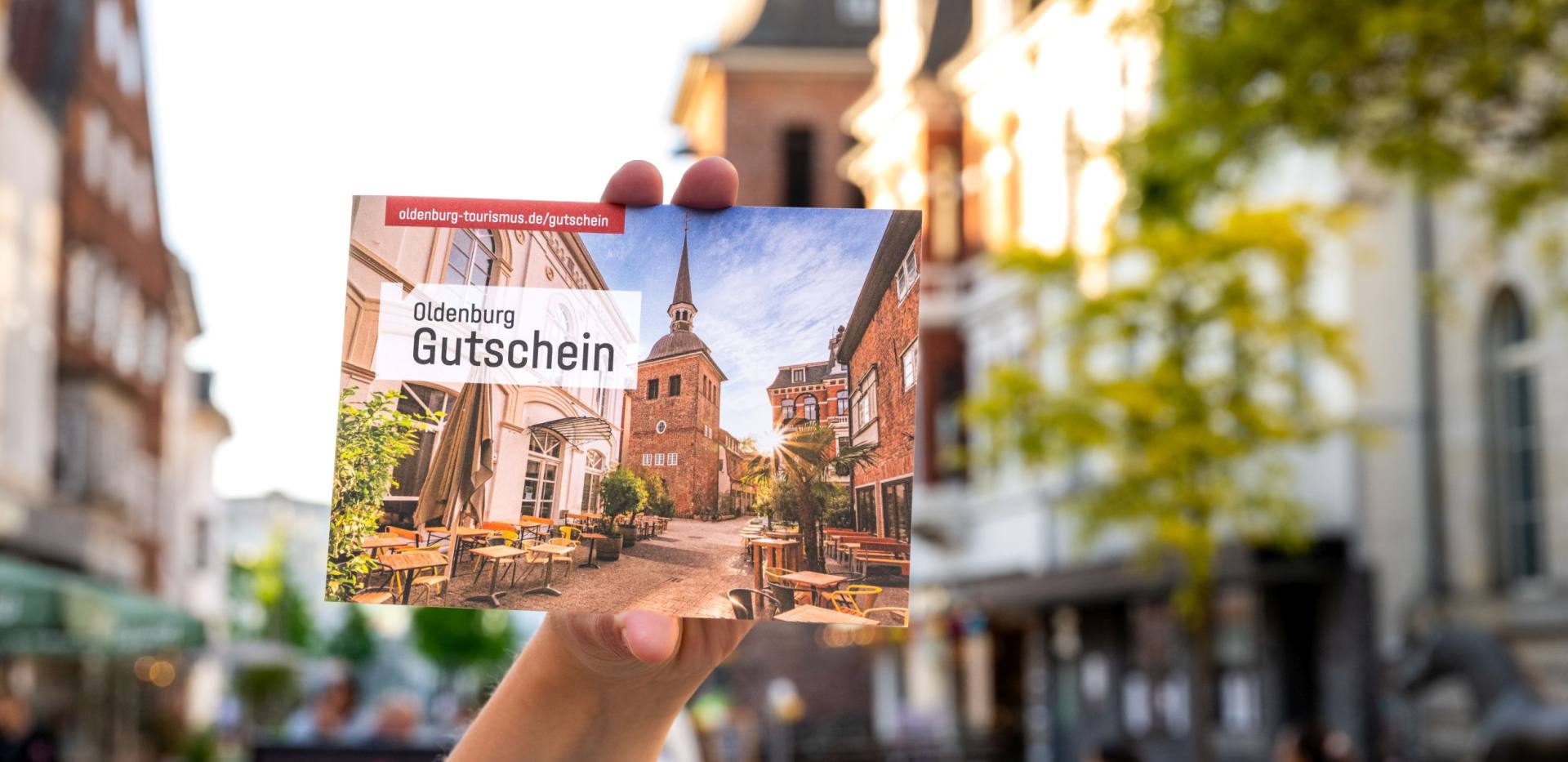 Eine Hand hält den Oldenburg Gutschein. Im Hintergrund die Oldenburger Fußgängerzone. Eine Hand hält den Oldenburg Gutschein. Im Hintergrund die Oldenburger Fußgängerzone.