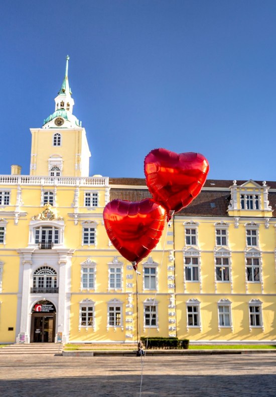 Blick auf das Schloss Oldenburg mit Herzluftballons davor.