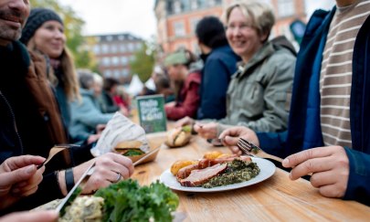 Menschen sitzen zusammen an einer Bierzeltgarnitur und Essen verschiedene Gr&uuml;nkohlgerichte. 