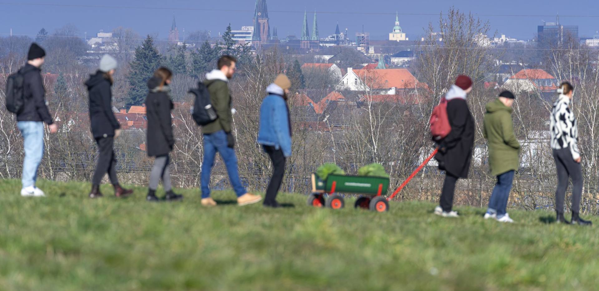 Eine Gruppe Menschen während einer Kohlfahrt mit einem Bollerwagen auf einer Landstraße. Im Hintergrund ist Oldenburg zu sehen. 