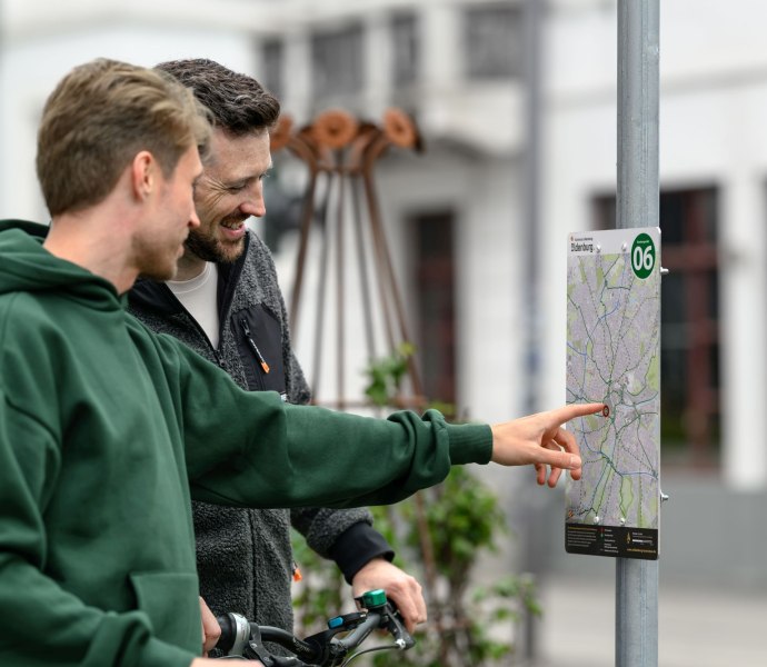 Zwei Radfahrer suchen sich auf einer Karte ihre Route durch das Knotenpunktsystem der Stadt aus. Zwei Radfahrer suchen sich auf einer Karte ihre Route durch das Knotenpunktsystem der Stadt aus.