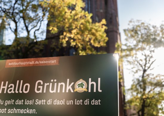 Hinweistafel zu "Hallo Grünkohl" mit Website für Detailinfos und plattdeutschem Spruch.  Hinweistafel zu