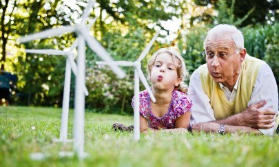 Ein Opa spielt mit seiner Enkelin mit einem Windparkmodell.