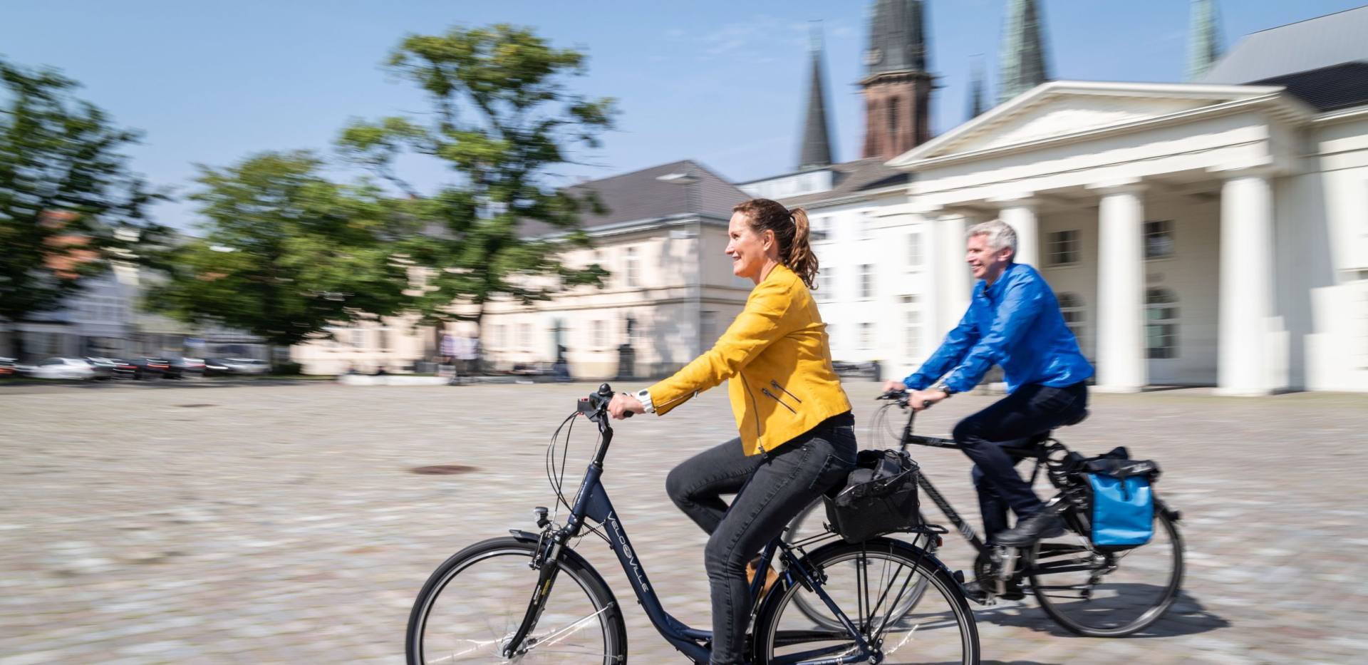 Eine Frau und ein Mann fahren mit dem Fahrrad über den Schlossplatz in Oldenburg. 