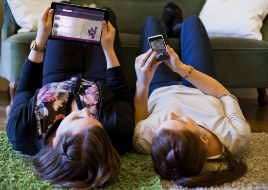 Zwei Freundinnen liegen nebeneinander auf dem Boden und informieren sich mit der Oldenburg-App.