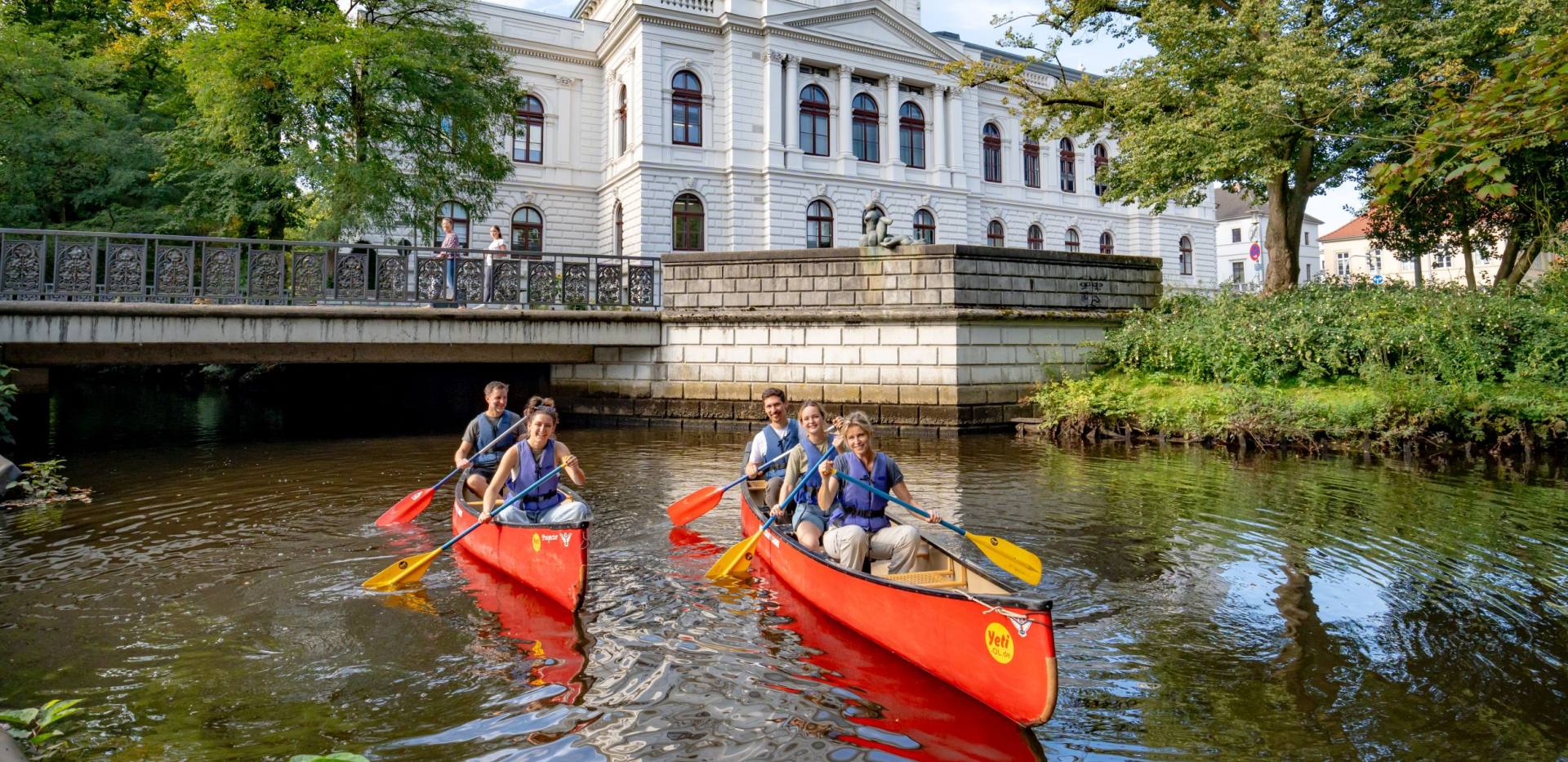 Zwei Kanus mit Stadtführungs-Teilnehmern, die „City Paddeln“ machen. Sie fahren auf der Hausbäke vor dem Oldenburgischen Staatstheater.