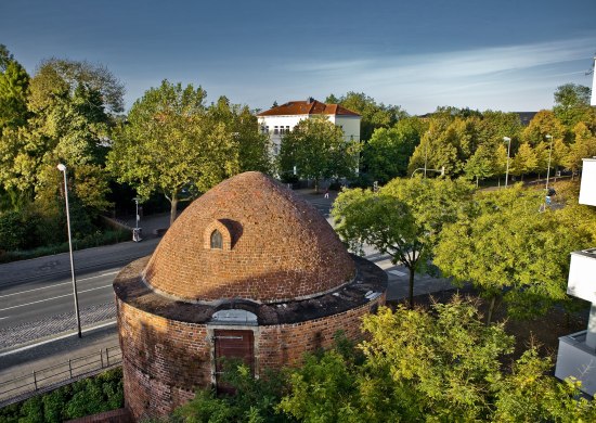 Blick auf den mittelalterlichen Pulverturm mit Stadthaus und Bäumen im Hintergrund.