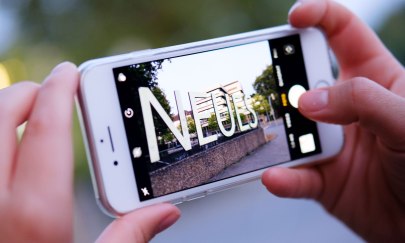 Schriftzug "Neues" vor dem Horst-Janssen-Museum aufgenommen als Blick durch ein Smartphone.