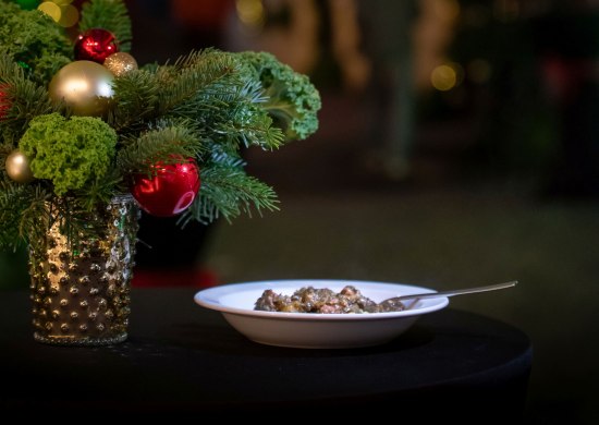 Ein Teller mit Grünkohleintopf neben einem Adventsgesteck und dem weihnachtlich geschmückten Lappangang in Oldenburg.