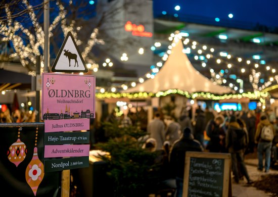 Skandinavisches Weihnachtsdorf Oldenburg Schild Skandinavisches Weihnachtsdorf Oldenburg mit beleuchtetem Markt im Hintergrund