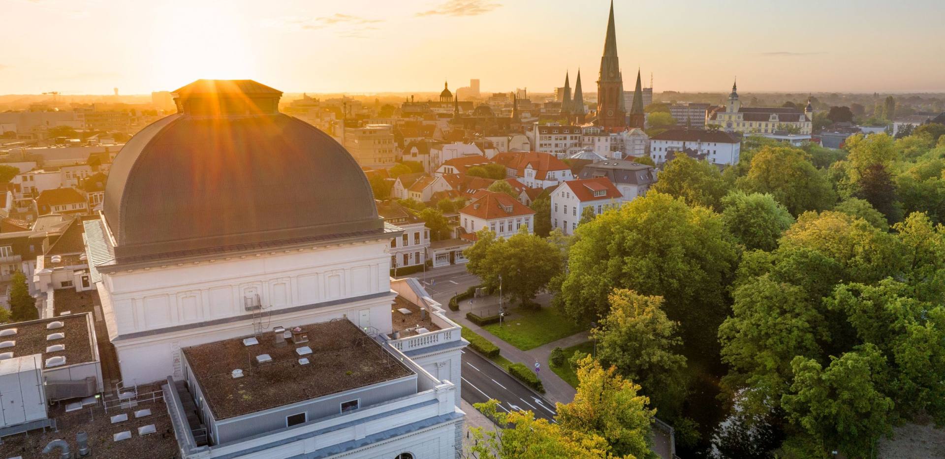 Sonne über den Dächern von Oldenburg mit Kuppel des Oldenburgischen Staatstheaters im Vordergrund.