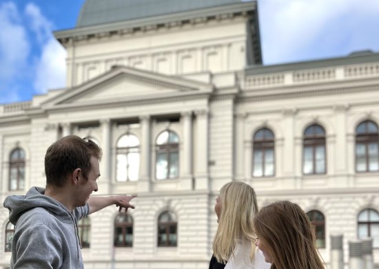 Drei junge Menschen unternehmen den rätselreichen Stadtrundgang und schauen sich vor dem Oldenburgischen Staatstheater und beantworten im begleitenden Heft eine Frage.