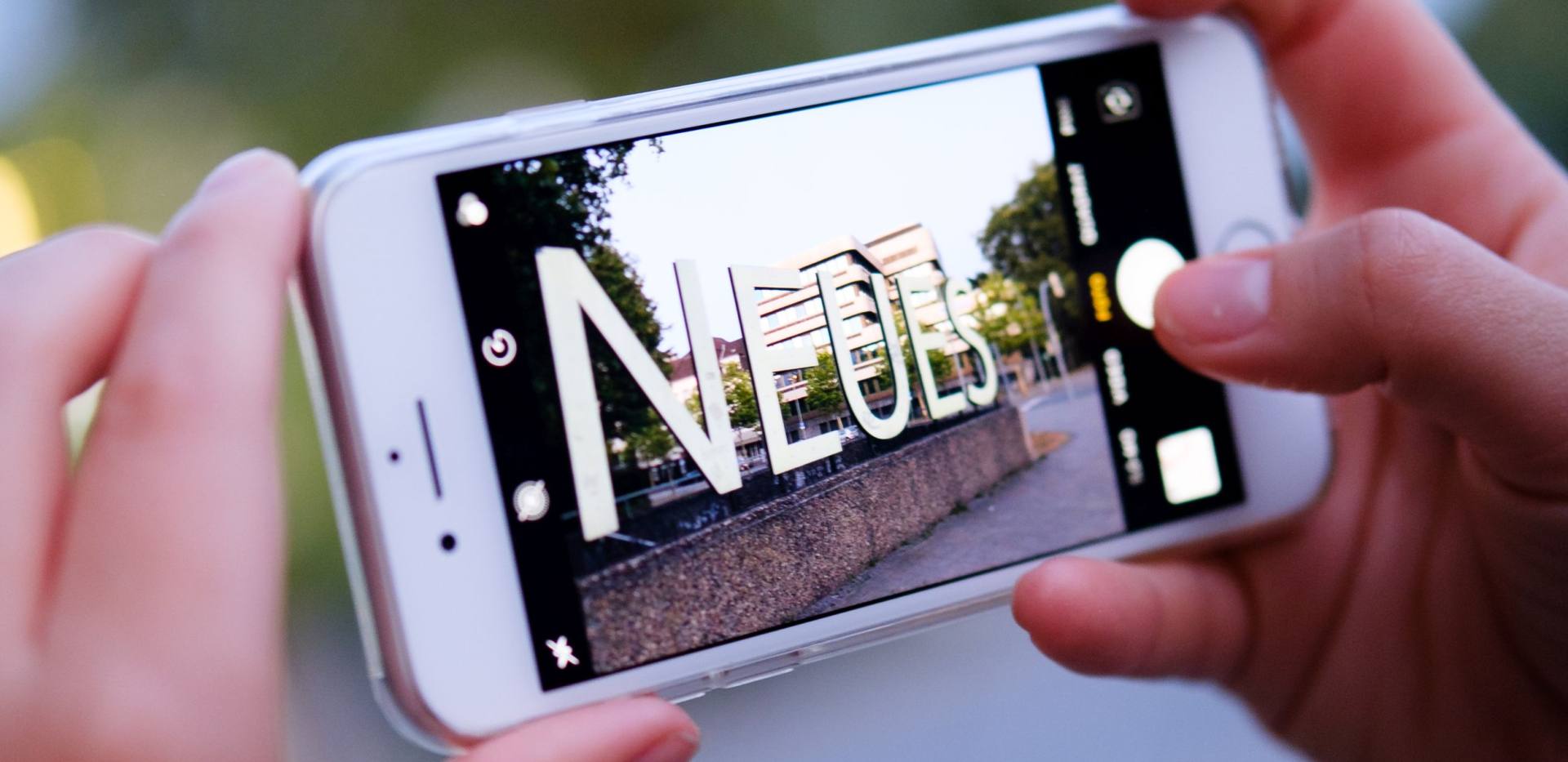 Schriftzug "Neues" vor dem Horst-Janssen-Museum aufgenommen als Blick durch ein Smartphone.