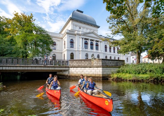 Zwei Kanus mit Teilnehmenden der Stadtf&uuml;hrung &bdquo;City Paddeln&ldquo;. Sie fahren auf der Hausb&auml;ke vor dem Oldenburgischen Staatstheater.