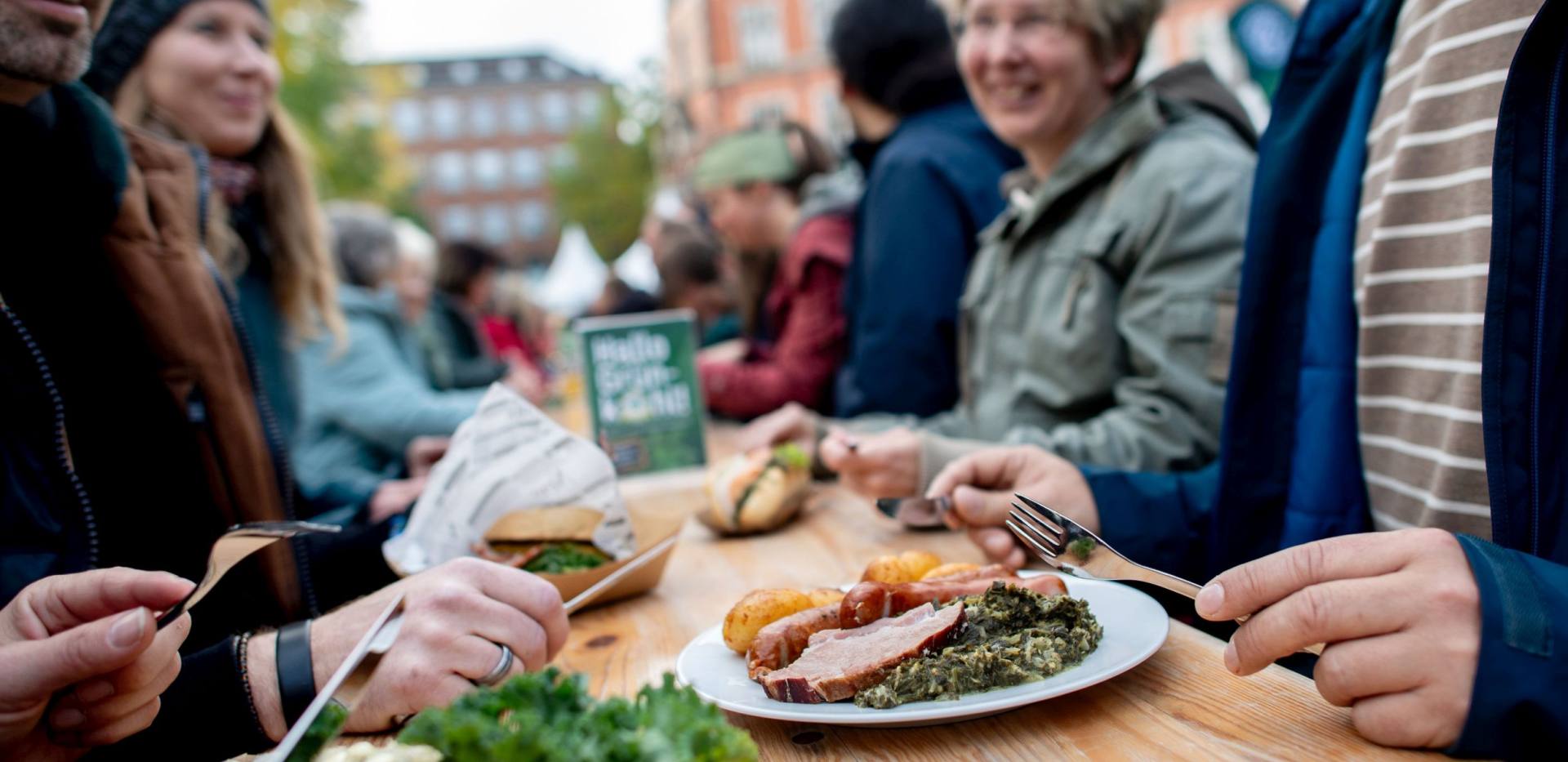 Menschen sitzen zusammen an einer Bierzeltgarnitur und Essen verschiedene Grünkohlgerichte. Menschen sitzen zusammen an einer Bierzeltgarnitur und Essen verschiedene Grünkohlgerichte.