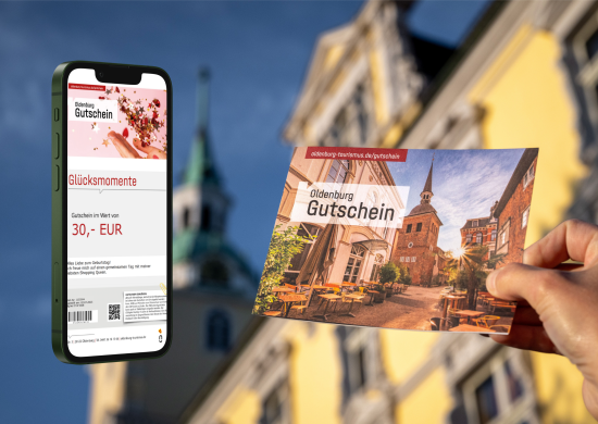 Klappkarte des Oldenburg-Gutscheins vor dem Schloss und Smartphone daneben mit Bild eines digitalen Gutscheins. 