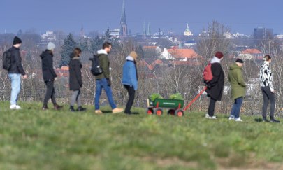 Eine Gruppe Menschen während einer Kohlfahrt mit einem Bollerwagen auf einer Landstraße. Im Hintergrund ist Oldenburg zu sehen. 