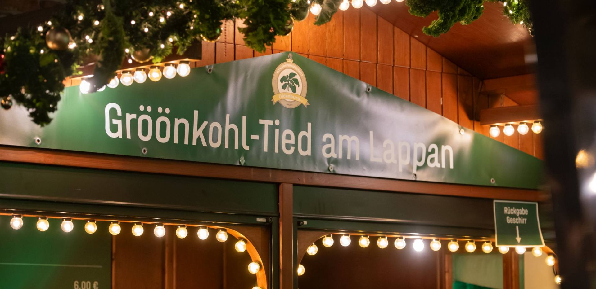Schild an der Holzbude "Gr&ouml;&ouml;nkohl-Tied am Lappan" und Weihnachtsschmuck.