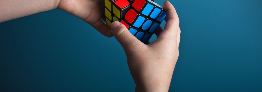 Zwei Händen drehen einen Zauberwürfel mit den Farben rot, gelb, blau Zwei Händen drehen einen Zauberwürfel mit den Farben rot, gelb, blau