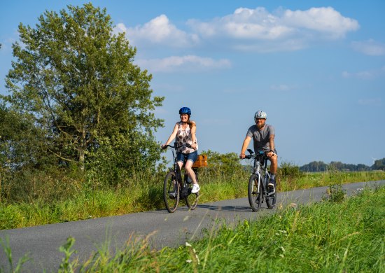 Ein radfahrendes Pärchen auf einem Radweg in der Wesermarsch. Die RadPartie ist eine DIY-Fotoerlebnistour durch Oldenburg und die Wesermarsch.