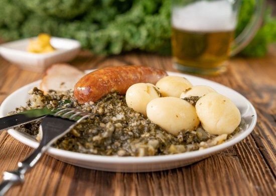 Tellergericht mit Grünkohl, Pinkel, Kassler und Kartoffeln. Tellergericht mit Grünkohl, Pinkel, Kassler und Kartoffeln. Im Hintergrund ein Bier und eine Schale mit Senf.